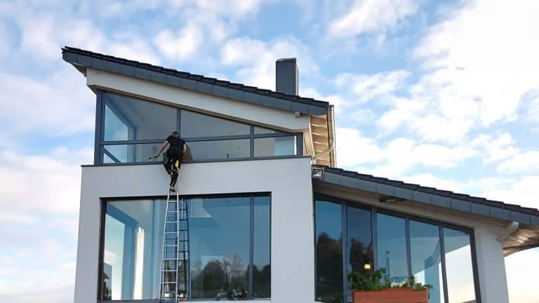 Daniel Klüßendorf steht auf einer Leiter und reinigt ein Fenster eines Gebäudes